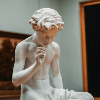 Escultura em pedra de alguém com os dedos da mão direita tocando em queixo